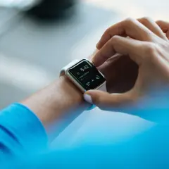 Dłoń dotyka ekranu smartwatcha, który pokazuje czas i krokomierz.