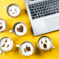 Kawa z emotikonami i kciukiem w górę obok laptopa. Chcesz wiedzieć, jak sprawdzić odznaki na FB?