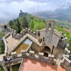 Widok z góry na kamienne fortyfikacje i wieże podczas san marino roaming. W oddali widać mgliste wzgórza i miasteczko.
