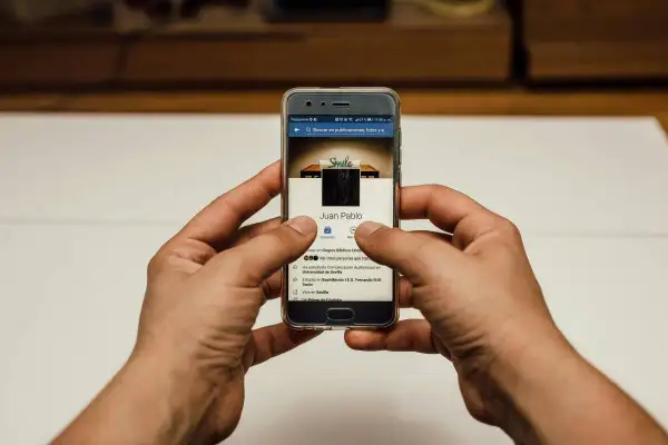 Ręce trzymają telefon z profilem FB. Chcesz wiedzieć, jak zmienić zdjęcie profilowe na FB, żeby nikt nie lajkował?