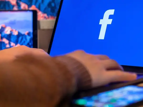 Dłoń na klawiaturze laptopa, na ekranie logo Facebooka. Dowiedz się, jak utworzyć stronę na Facebooku.