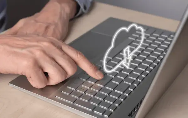 Dłoń naciska klawisz na laptopie, nad którym unosi się symbol chmury internetowej z ikoną pobierania.
